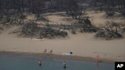 People play with a ball in front of a burnt forest at a beach, near Gennadi village, on the Aegean Sea island of Rhodes, southeastern Greece, July 27, 2023. 