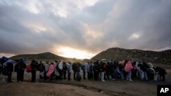 FILE - Asylum-seeking migrants line up in a makeshift, mountainous campsite to be processed after crossing the border with Mexico, Feb. 2, 2024, near Jacumba Hot Springs, California.