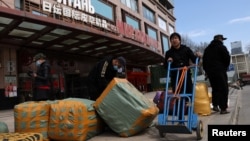 FILE - Men move bags of goods for export in front of a trading center that houses shops and offices with Russian goods and services, in Beijing, April 1, 2022.