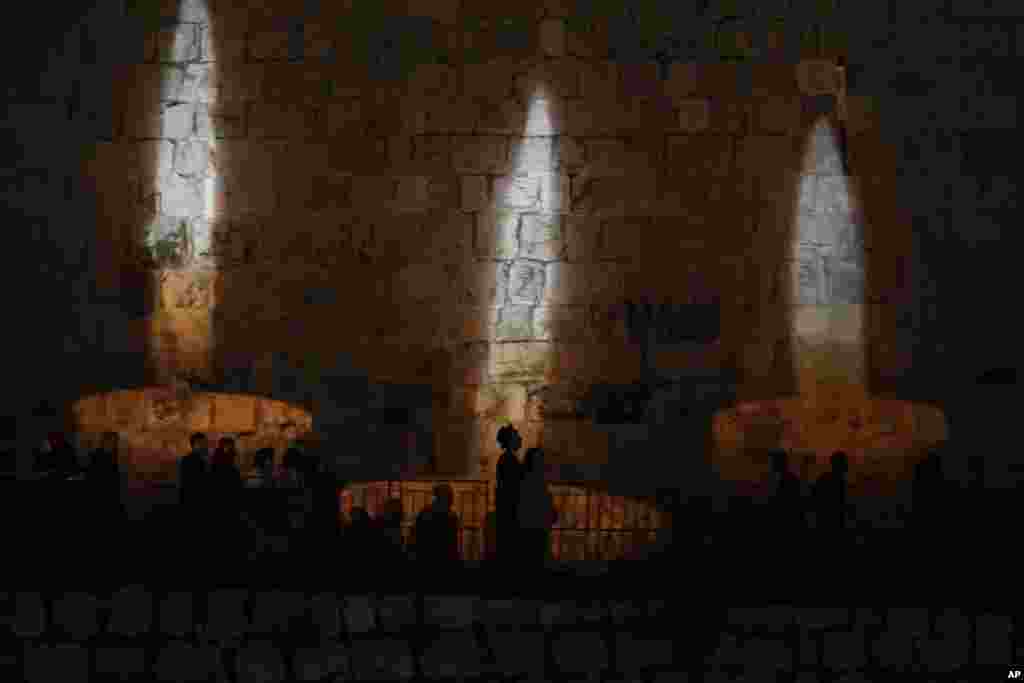 People walk by an image of memorial candles, projected on the walls of Jerusalem's Old City on the eve of annual Holocaust Remembrance Day, April 17, 2023. 