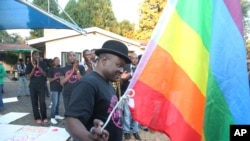 FILE - Samba Chesterfield, Director of Gays and Lesbians Association of Zimbabwe, prepares to hoist their official flag alongside the Zimbabwean flag during during an event in Harare, Zimbabwe on Saturday, May, 19, 2012.