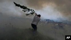 FILE - A volunteer uses a tree branch trying to prevent a forest fire from reaching houses in the village of Casal da Quinta, outside Leiria, central Portugal, July 12, 2022.