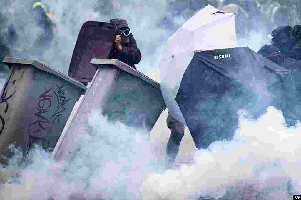 Protesters protect themselves from tear gas smoke behind umbrellas and garbage containers during clashes on the sidelines of a demonstration on the 11th day of action after the government pushed a pensions reform through parliament without a vote, using the article 49.3 of the constitution, in Nantes, western France.