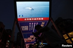 FILE - A screen broadcasts news footage of a Navy Force vessel taking part in military drills by the Eastern Theatre Command of China's People's Liberation Army around Taiwan, in a shopping area in Beijing, Aug. 19, 2023.