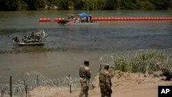 Guardsmen patrol as workers deploy large buoys to be used as a border barrier along the banks of the Rio Grande in Eagle Pass, Texas, July 12, 2023.