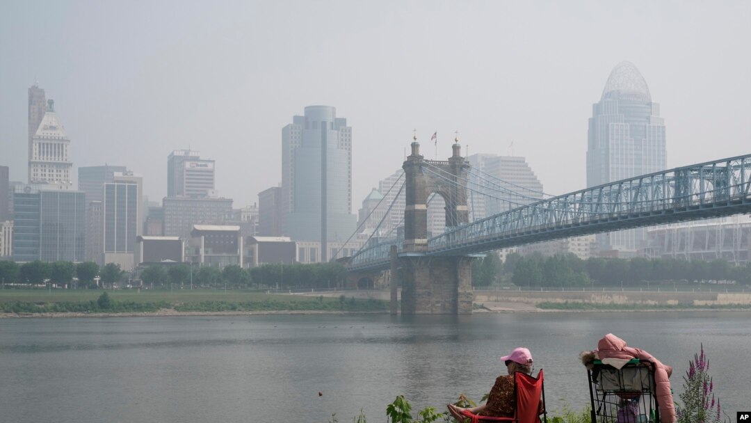 Seseorang duduk di dekat Sungai Ohio saat asap dari kebakaran hutan terlihat di pusat kota Cincinnati, Rabu, 28 Juni 2023. (AP/Joshua A. Bickel)