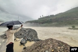 In this photograph taken on July 9, 2023, a man holds an umbrella while standing on the banks of swollen river Satluj after heavy monsoon rains in Rampur, in India's Himachal Pradesh state. (Photo by AFP)