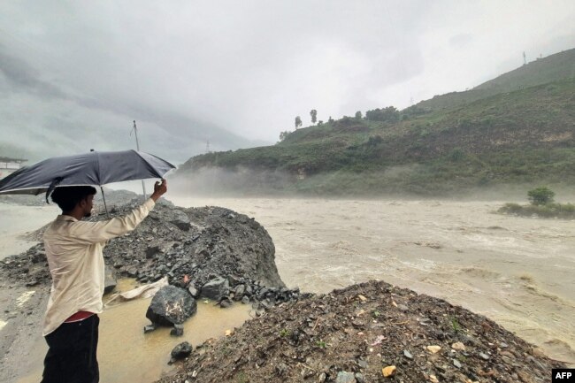 In this photograph taken on July 9, 2023, a man holds an umbrella while standing on the banks of swollen river Satluj after heavy monsoon rains in Rampur, in India's Himachal Pradesh state. (Photo by AFP)