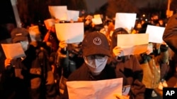 FILE - Protesters hold up blank papers and chant slogans as they march in protest in Beijing, Nov. 27, 2022.
