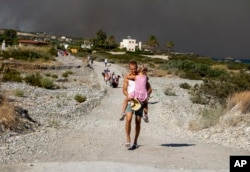 Čovek nosi dete dok napušta oblast šumskih požara, na ostrvu Rodos, Grčka, 22. jula 2023.