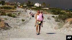 A man carries a child as they leave an area where a forest fire burns, on the island of Rhodes, Greece, July 22, 2023.
