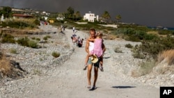 A man carries a child as they leave an area where a forest fire burns, on the island of Rhodes, Greece, July 22, 2023. 