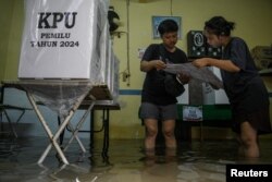 Petugas pemilu memeriksa surat suara di TPS pemilu yang terendam banjir di Duri Kepa, Kebon Jeruk, Jakarta, 14 Februari 2024. (Antara Foto/Sulthony Hasanuddin via REUTERS)