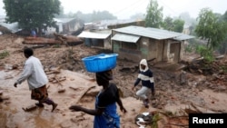 People walk past homes damaged by Cyclone Freddy in Chilobwe, Malawi, March 17, 2023.
