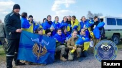 Combatientes ucranianos posan, muchos de ellos arropados con la bandera de su país, tras ser liberados por Rusia en un intercambio de prisioneros de guerra, en una ubicación desconocida, el 10 de abril de 2023.