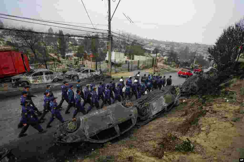 Chilean Navy workers walk past overturned, burned cars as they deploy to help aid the Villa Independencia neighborhood affected by forest fires in Vina del Mar.