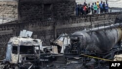 Orang-orang berdiri di dinding bangunan yang rusak untuk melihat puing-puing bagasi dan kapal tanker yang terbakar, sehari setelah ledakan gas menyebabkan kerusakan parah di kawasan Embakasi, Nairobi, 2 Februari 2024. (LUIS TATO / AFP)