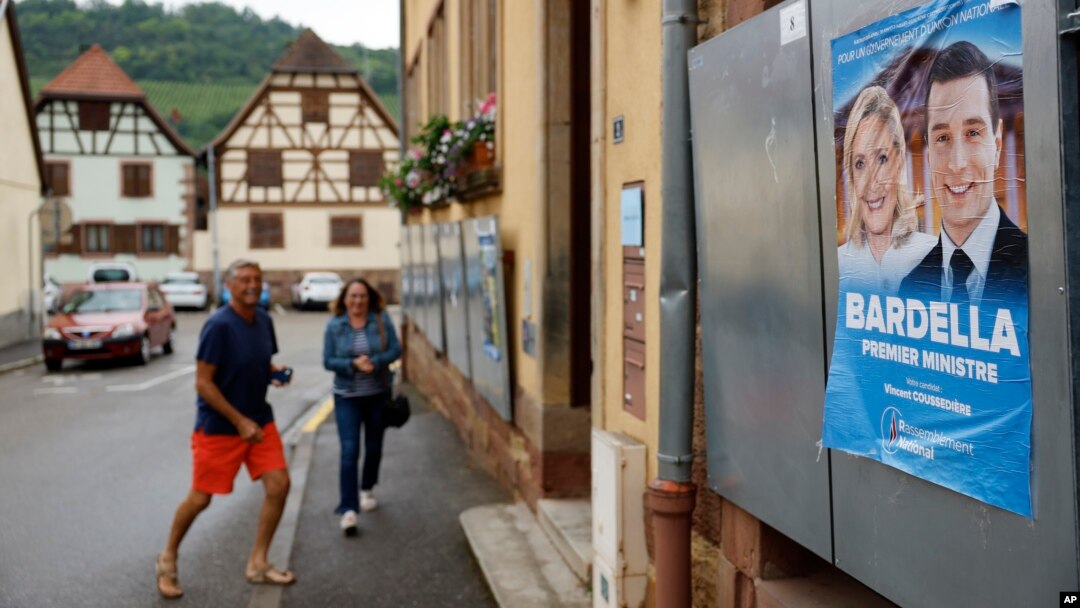 Glasači stižu na biračko mjesto u Soultz-Les-Bainsu, istočna Francuska, 30. juna 2024. Poster s francuskim liderima krajnje desnice Marine Le Pen i Jordanom Bardellom vidi se na desnoj strani.