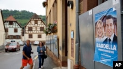 Voters arrive at a polling station in Soultz-Les-Bains, eastern France, June 30, 2024. A poster with French far-right leaders Marine Le Pen and Jordan Bardella is seen on the right.