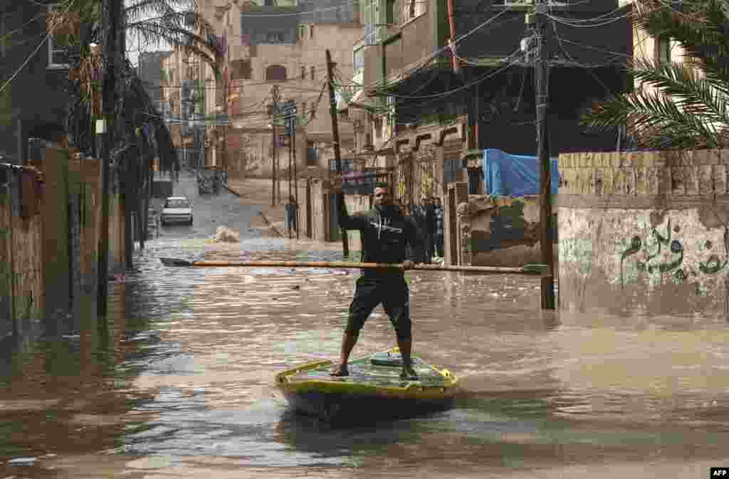 A Palestinian man rides a paddle board on a flooded street following heavy rain at the Al-Shati refugee camp in the Gaza strip.
