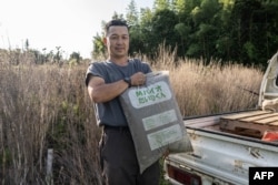 Nobuyoshi Fujiwara, seorang pemilik kebun selada, berpose dengan sekantong pupuk buatan kotoran manusia (shimogoe) di kebunnya di kota Yokosuka, prefektur Kanagawa, 13 Juni 2023. (Yuichi YAMAZAKI/AFP)