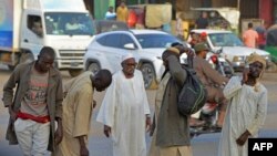 Hombres caminan por una calle en la ciudad gemela de Umdurman en Jartum, el 16 de abril de 2023, el ejército de Sudán y los paramilitares rivales comenzaron una pausa humanitaria de una hora en el segundo día de batallas urbanas.