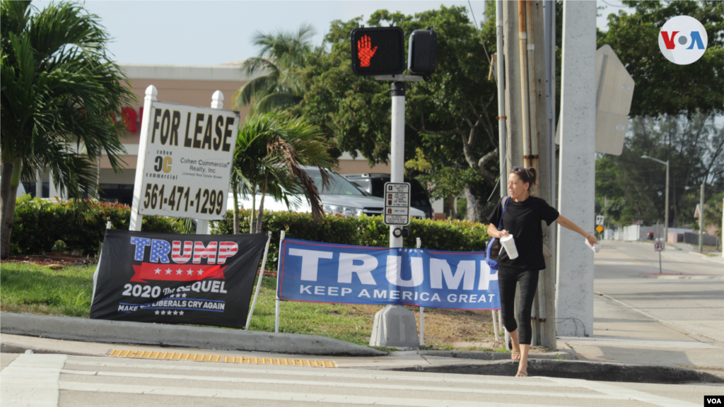 Una residente de Palm Beach cruza una calle donde se pueden ver pancartas en apoyo al expresidente Donald Trump, el 3 de abril de 2023. 