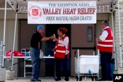 FILE - Salvation Army volunteer Francisca Corral, center, gives water to a man at a their Valley Heat Relief Station, July 11, 2023 in Phoenix, Arizona.