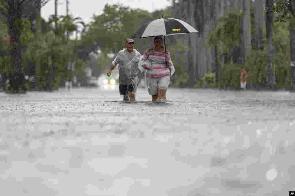 Una pareja camina por la calle Arthur mientras fuertes lluvias inundan el vecindario circundante en Hollywood, Florida.