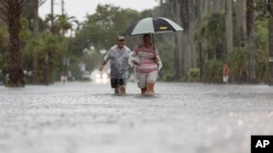 Jim Comunale y Pam Mervos caminan por Arthur Street mientras las fuertes lluvias inundan el vecindario circundante el miércoles 12 de junio de 2024 en Hollywood, Florida.