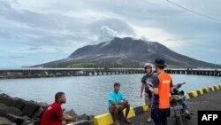 Seorang anggota Basarnas berbicara dengan warga di Sitaro, Sulawesi Utara dengan latar belakang gunung berapi Gunung Ruang yang mengeluarkan asap, 18 April 2024. (Handout / Badan Pencarian dan Pertolongan Nasional (BASARNAS) / AFP)
