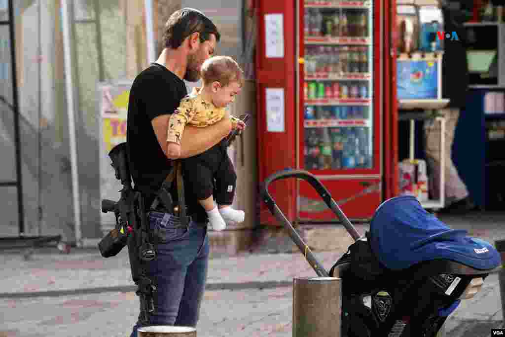 Un hombre armado con una pistola y un rifle de asalto pasea con su hijo por Jerusalén a pocas horas del inicio del cese al fuego pactado entre Israel y Hamás.