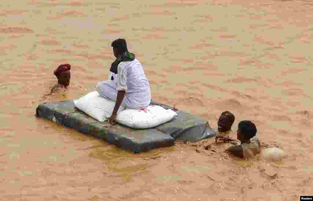 A person sits on bags of aid on a makeshift raft while others wade through flood water, following devastating floods, in South Tokar, Red Sea State, Sudan.