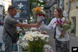 A woman buys bouquets of flowers at a street flower stall in Kyiv, Ukraine, June 25, 2024.