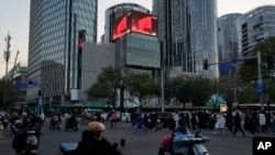 FILE - Residents pass near a commercial district with a screen showing the Chinese national flag in Beijing, Nov. 18, 2023. China's economic weakness appears to have made international investors wary. 