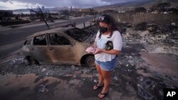 FILE - Summer Gerling picks up her piggy bank found in the rubble of her home following the wildfire on Aug. 10, 2023, in Lahaina, Hawaii.