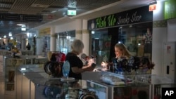 A seller shines a flashlight as she shows goods to a customer during a power outage in Kyiv, June 19, 2024. Russian regular massive missile attacks against Ukraine's energy facilities have resulted in electricity supply restrictions.