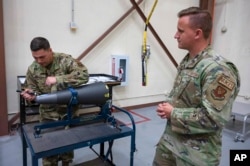 In this image provided by the U.S. Air Force, Staff Sgt. Brandon Mendola, left, with the 90th munitions squadron at F.E. Warren Air Force Base in Wyoming demonstrates how they train new missile maintainers to look for scratches on the top of a nuclear warhead.