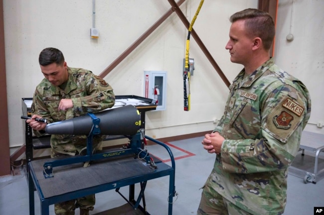 In this image provided by the U.S. Air Force, Staff Sgt. Brandon Mendola, left, with the 90th munitions squadron at F.E. Warren Air Force Base in Wyoming demonstrates how they train new missile maintainers to look for scratches on the top of a nuclear warhead.