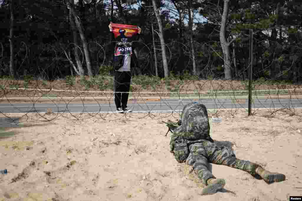 Seorang aktivis anti-perang mengangkat tanda &quot;Hentikan latihan perang, Pulanglah&quot; di depan seorang marinir Korea Selatan yang sedang mengambil posisi selama latihan pendaratan amfibi korps marinir AS dan Korea Selatan, di Pohang.