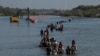 Una caravana pasa junto a una serie de boyas, que se construyen para disuadir a los migrantes de cruzar el río Grande, mientras buscan una abertura en el alambre de concertina para ingresar a Eagle Pass, Texas, EEUU, el 27 de julio de 2023.
