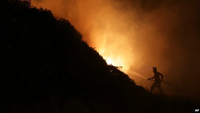 FILE - A volunteer uses a water hose to fight a wildfire near houses on the outskirts of Obidos, Portugal, early on Oct. 16, 2017.