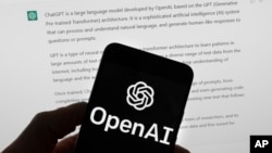 The OpenAI logo is seen on a mobile phone in front of a computer screen which displays output from ChatGPT, March 21, 2023, in Boston.(AP Photo/Michael Dwyer, File)
