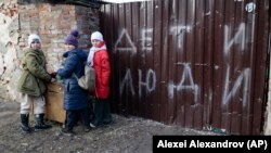 (FILE) Children stand near the fence of a damaged house with the words "Children and people" in Ukraine.