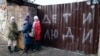 Дети стоят у забора разрушенного дома с надписью «Дети и люди» в Мариуполе 25 февраля 2023 года. (Алексей Александров/AP)