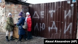 Дети стоят у забора разрушенного дома с надписью «Дети и люди» в Мариуполе 25 февраля 2023 года. (Алексей Александров/AP)