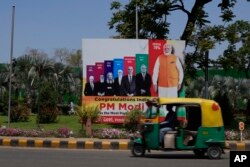 Sebuah becak melewati papan besar yang menunjukkan popularitas Perdana Menteri India Narendra Modi di antara potret para pemimpin dunia, di New Delhi, India, Kamis, 6 April 2023. (AP/Manish Swarup)