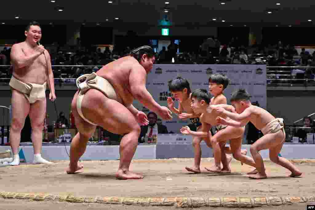 Retired Mongolian-born &quot;yokozuna&quot; wrestler Hakuho (far L) watches as participants (R) try to push out Japanese wrestler Hakuoho (C) during a sumo class for youngsters at the Kokugikan arena in the Ryogoku area of Tokyo.