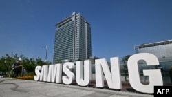 A worker waters the flower garden next to the logo of Samsung Electronics at the company's headquarters in Suwon on June 13, 2023. 