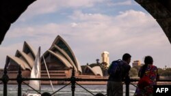 A couple watches boats as they stand on the harbor foreshore opposite the Sydney Opera House in Sydney on Oct. 1, 2023.